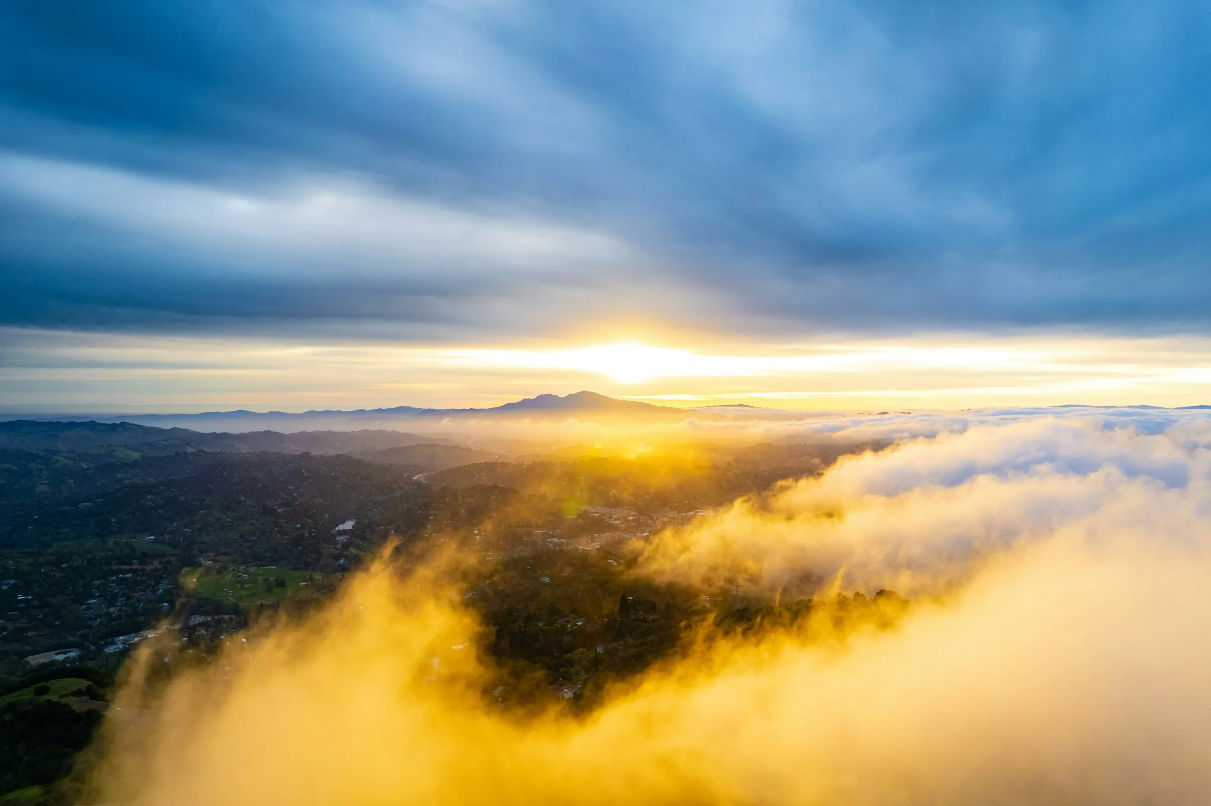 Sunrise breaking behind the twin peaks of Mount Diablo, with low cloud rolling across the valley and its neighbourhoods below.